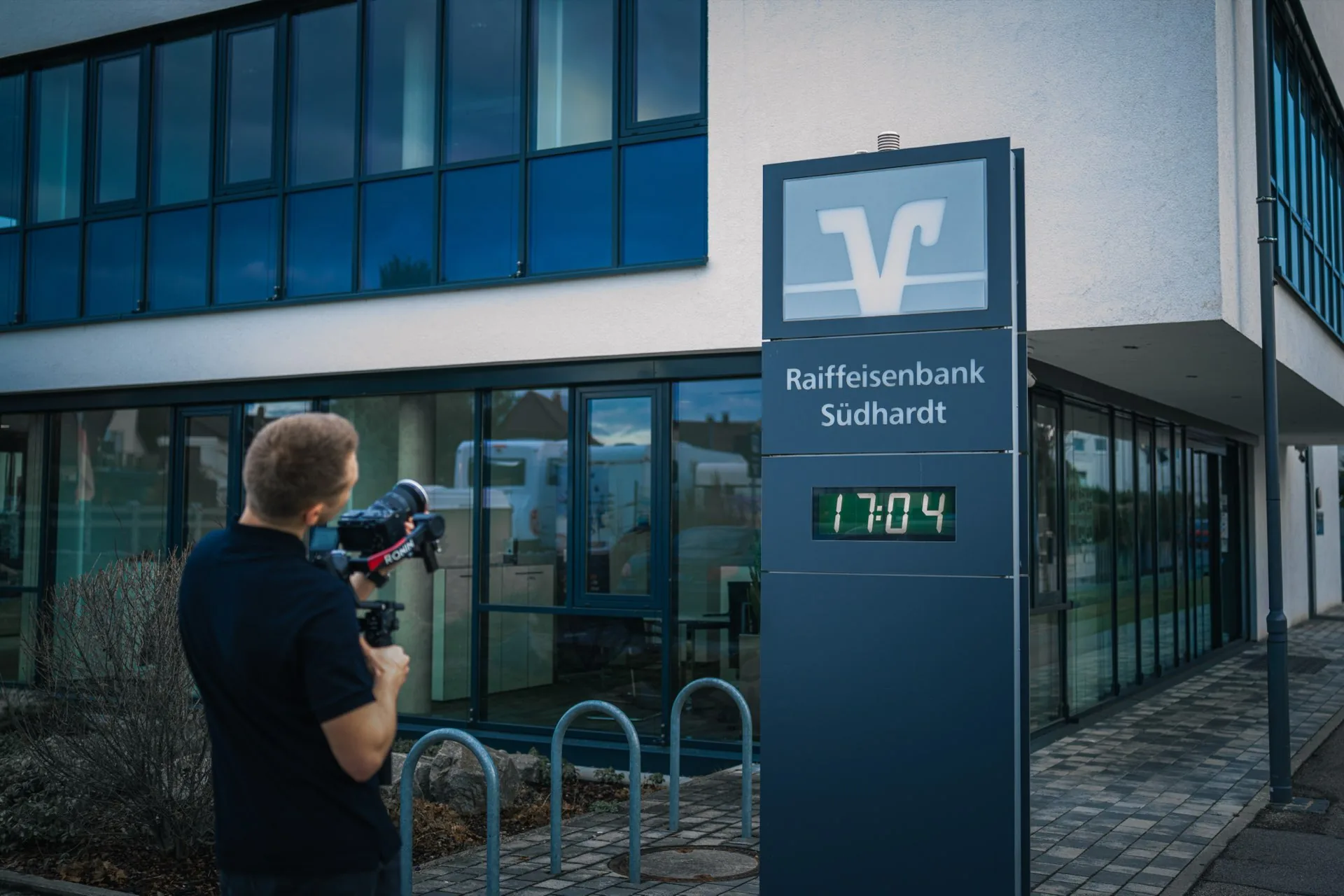 Kameramann filmt die Fassade der Raiffeisenbank Südhardt eG, die Uhr zeigt 17:04